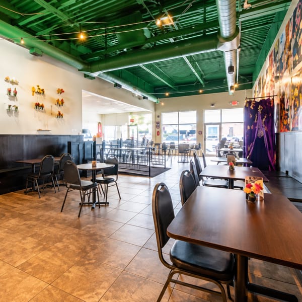 Spacious restaurant interior with dark tables, black chairs, a green ceiling, and vibrant wall art.
