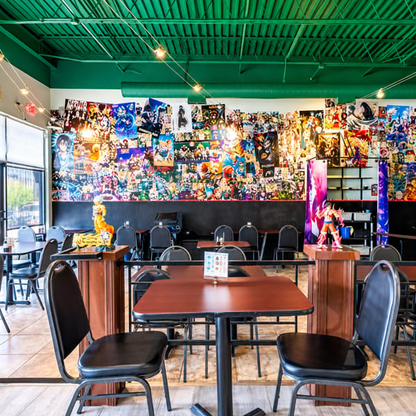 Colorful restaurant interior with a green ceiling, tables, chairs, and a wall covered in anime posters and figurines.