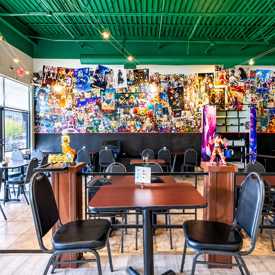 Colorful restaurant interior with a green ceiling, tables, chairs, and a wall covered in anime posters and figurines.