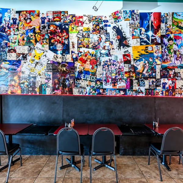 Anime-themed restaurant interior featuring a wall collage of manga art above black booths and tables.
