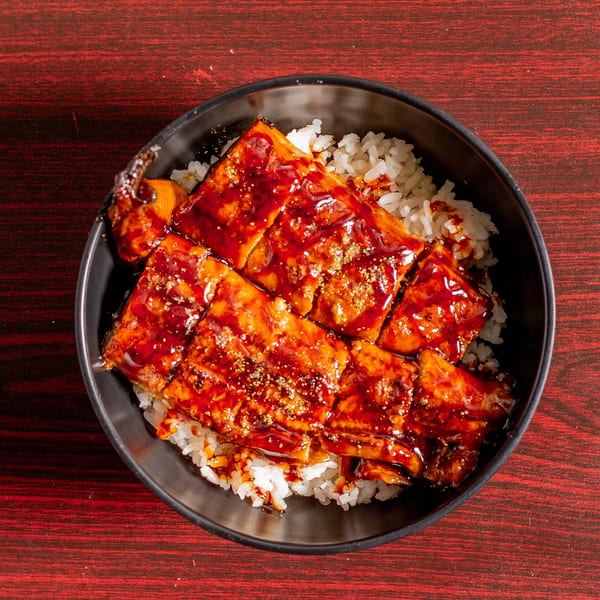 Unagi donburi, grilled eel with sweet soy glaze over white rice in a black bowl.